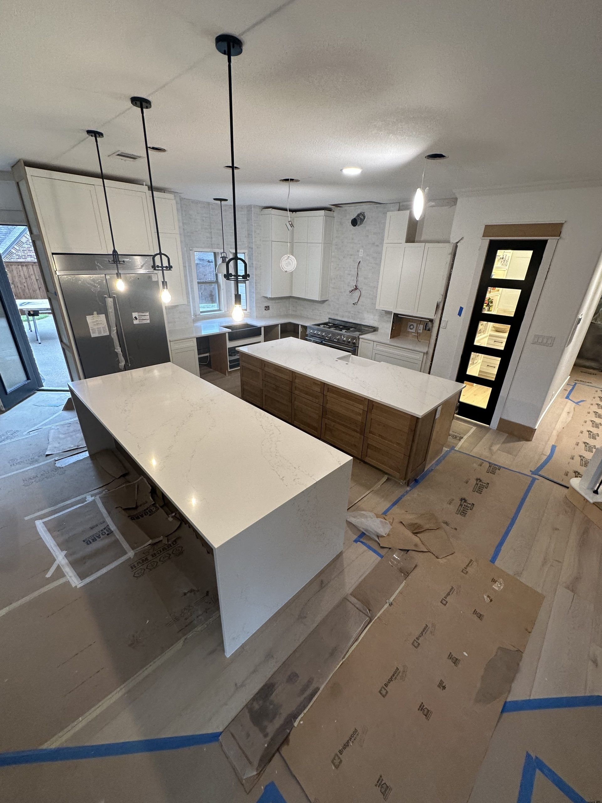 Modern kitchen under construction with two islands, light cabinets, and pendant lights.