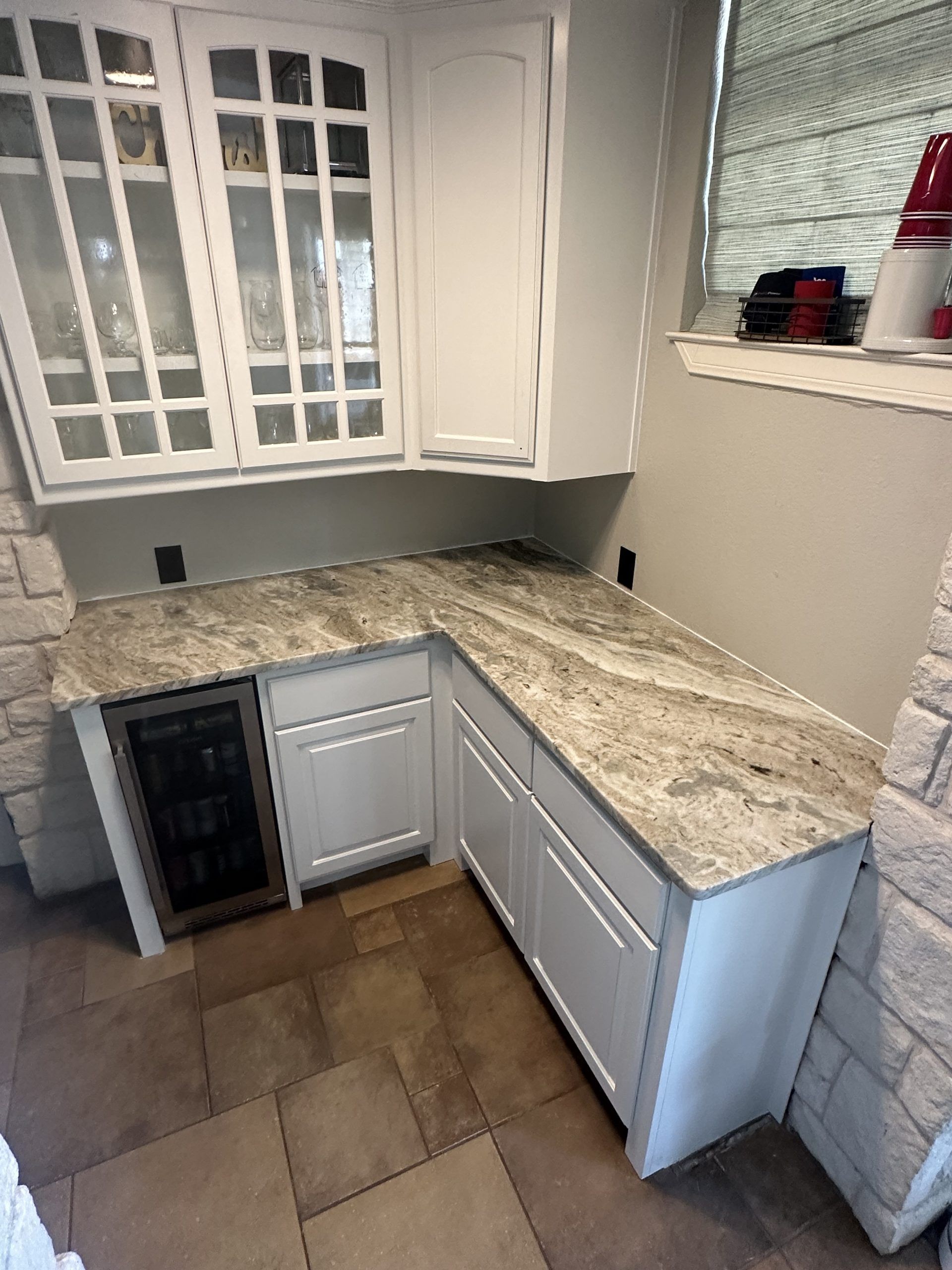 White kitchen cabinets and granite countertop in a corner, with a wine cooler and glass-front upper cabinets.