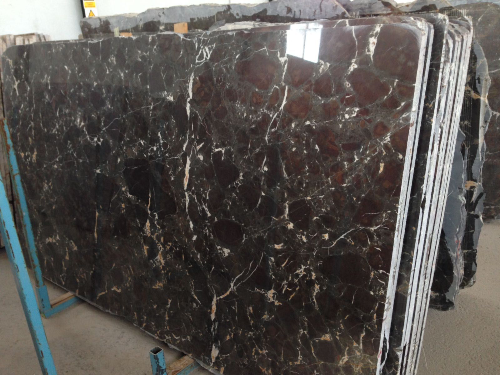 Stack of polished brown marble slabs with white veining, on a metal support.