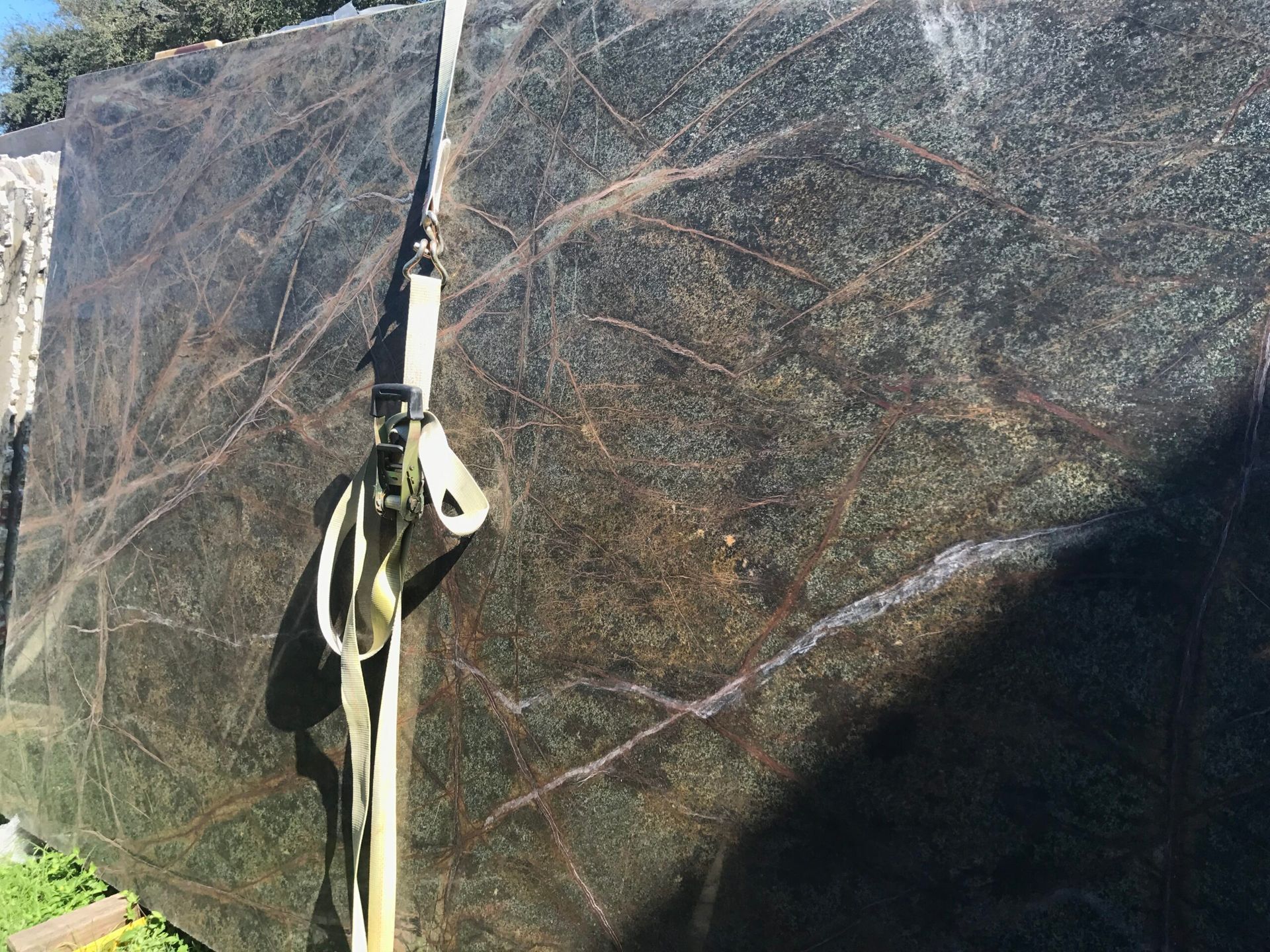 Large slab of green-black granite with gold and white veining, secured with straps.