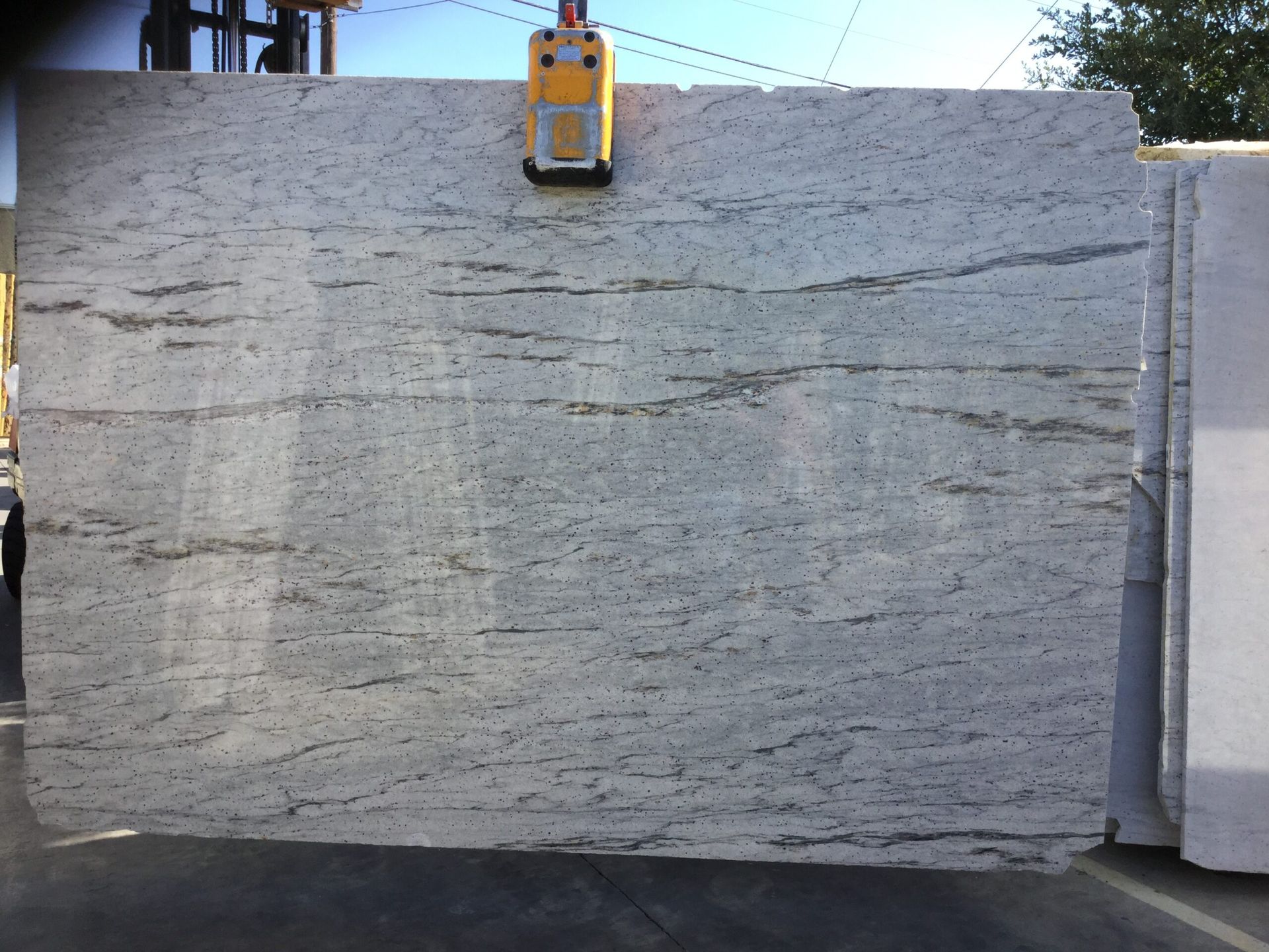 A large slab of white granite with gray veining being lifted by a yellow crane.