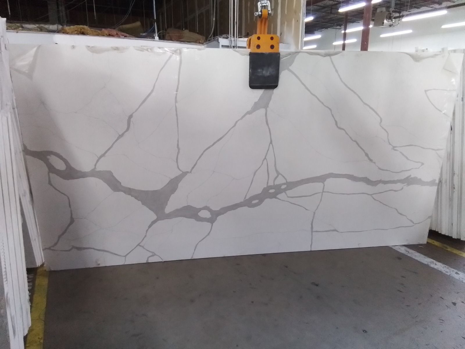 Large white quartz slab with gray veining being lifted by a crane in a warehouse.