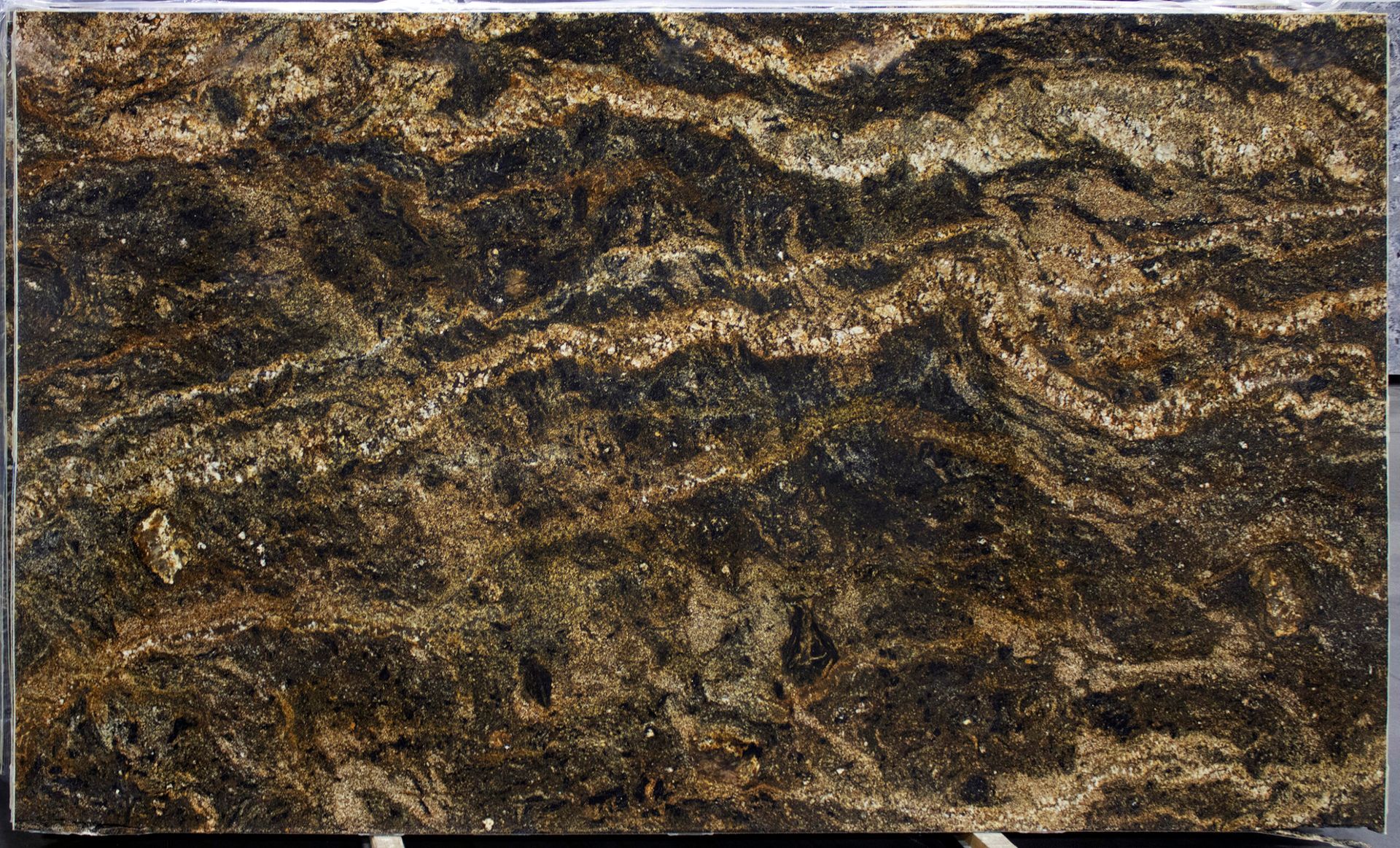 A dark brown and gold granite slab with wavy, swirling patterns.