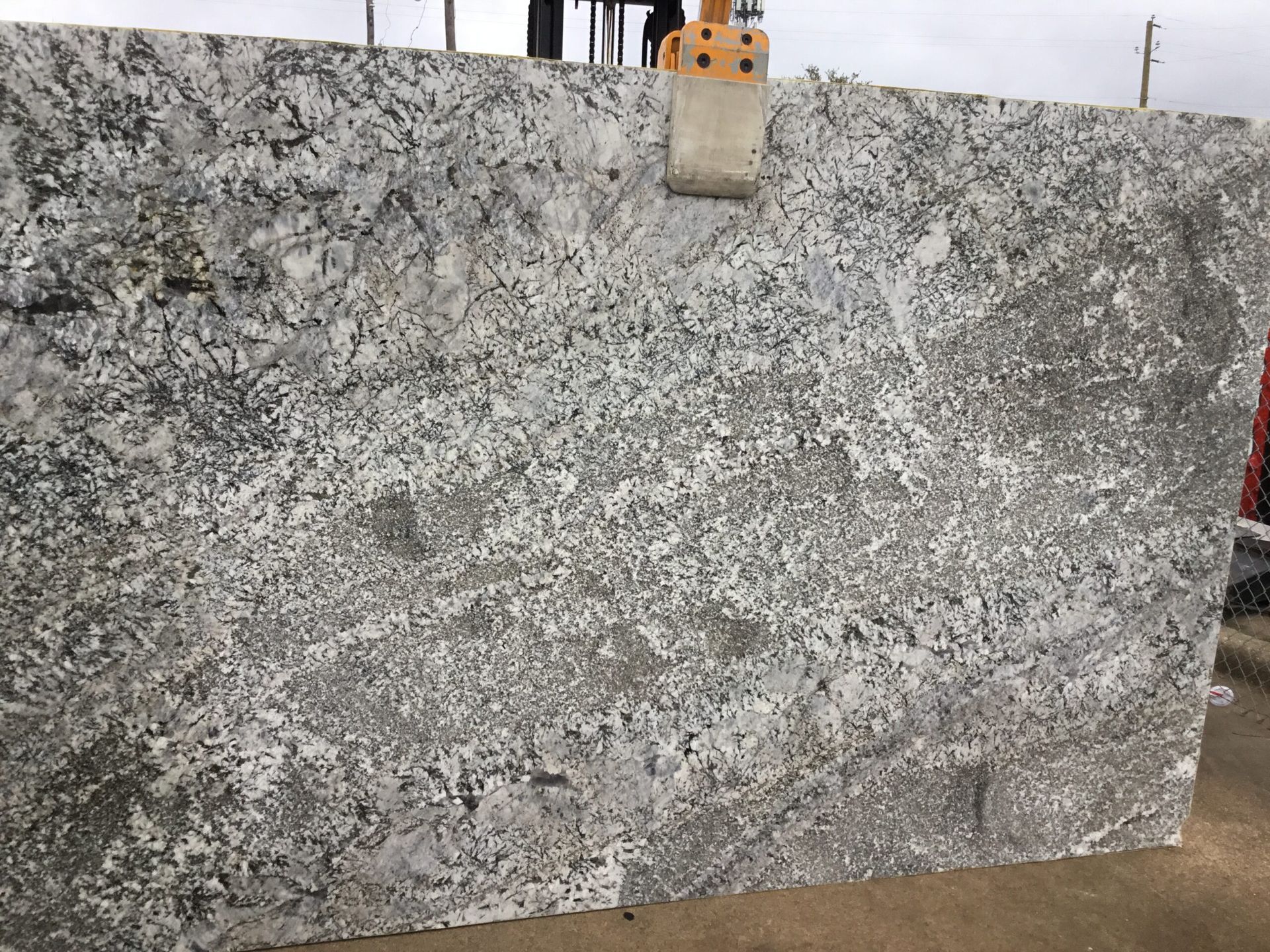 A large granite slab with a gray and white pattern, held by a forklift.