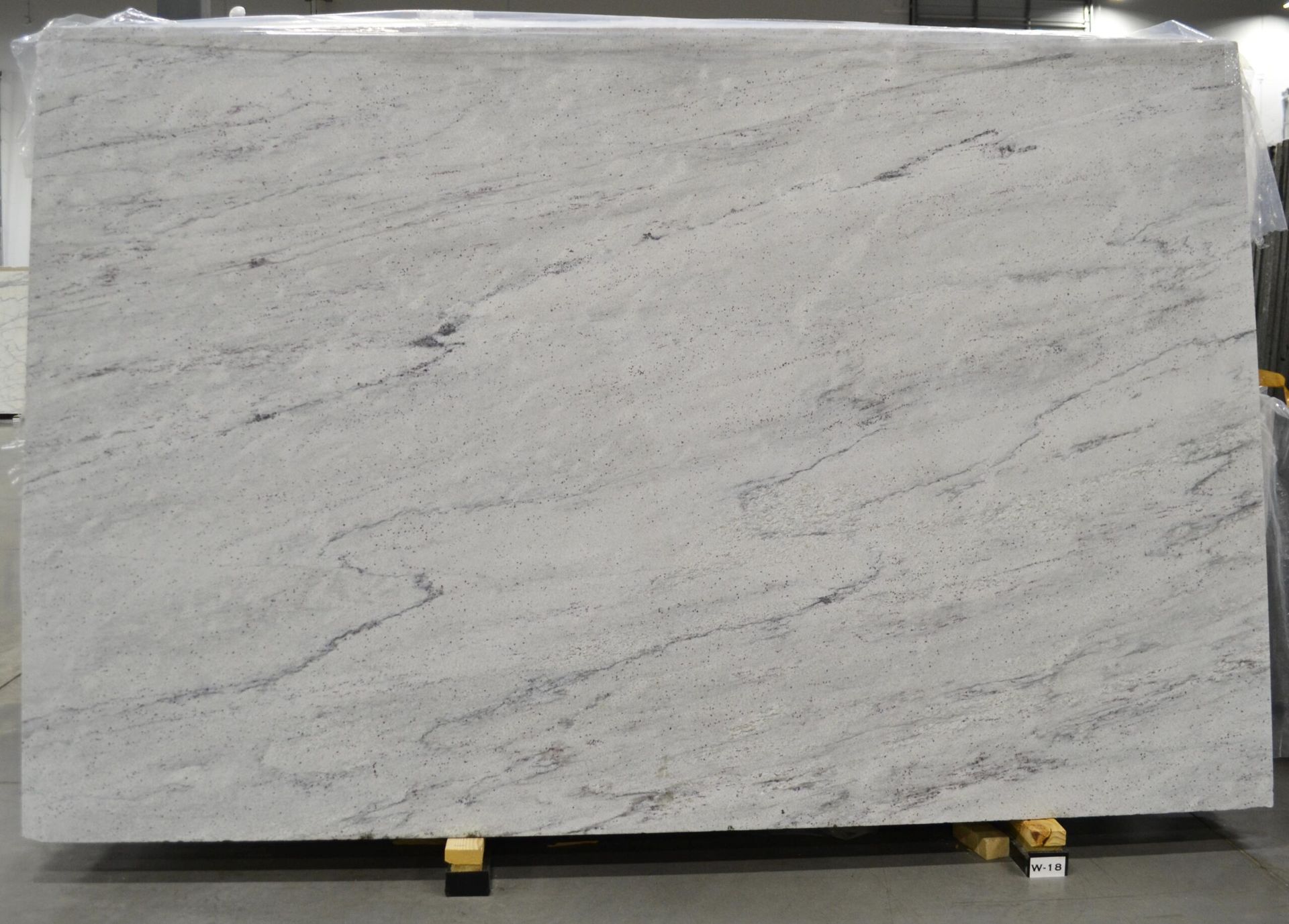 A large white granite slab with gray veining is displayed indoors on a wooden pallet.