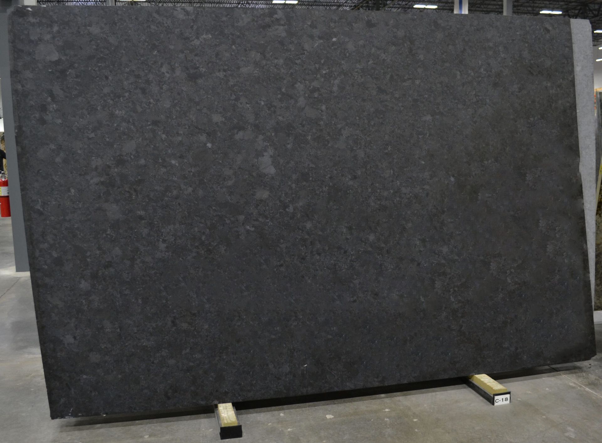 Large slab of dark gray granite leaning on a wooden rack in a warehouse setting.
