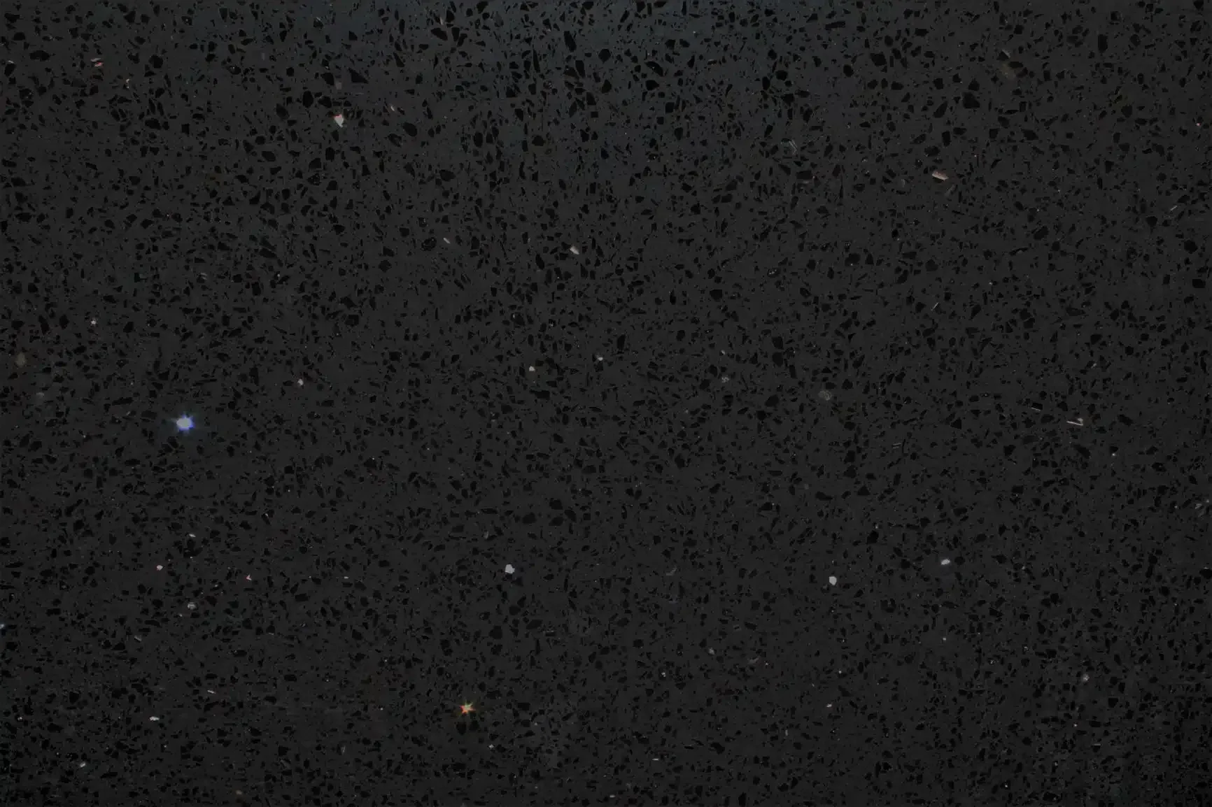 Black speckled surface with small bright dots, possibly a dark countertop or night sky.