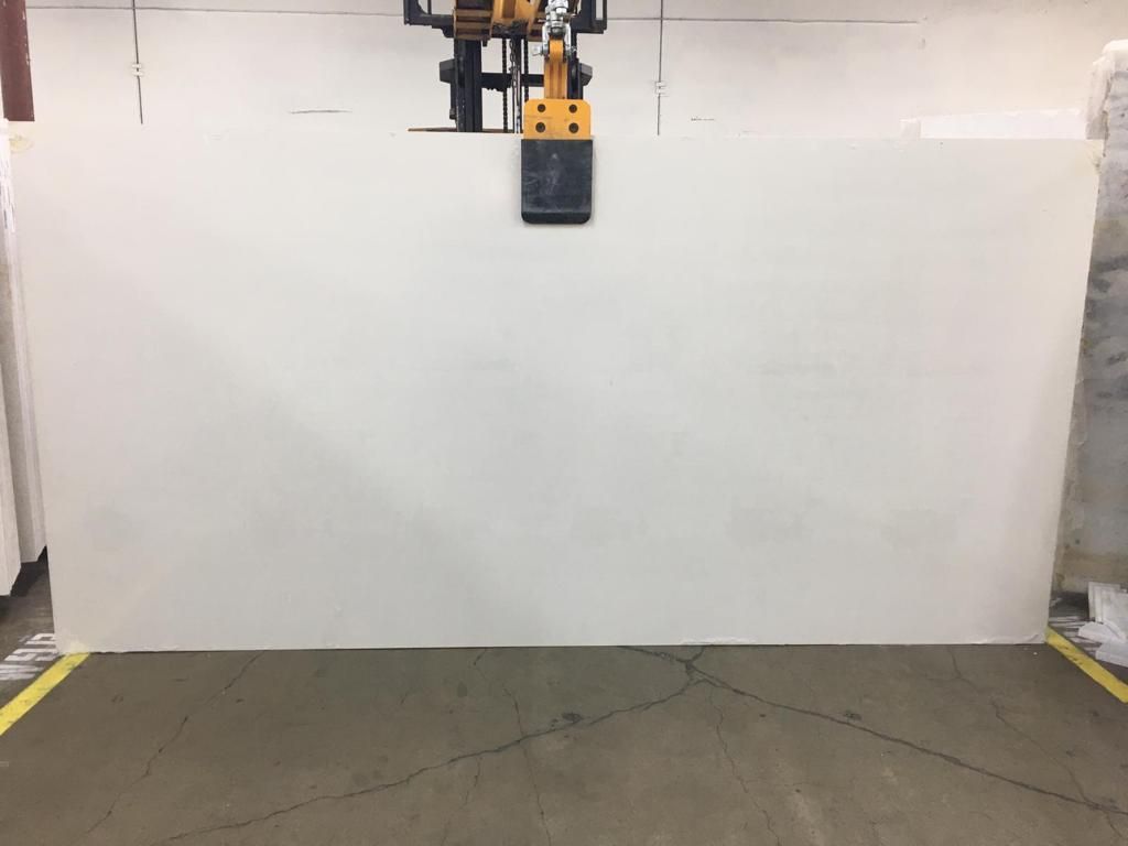 A large, white countertop slab being lifted by a forklift in a warehouse.
