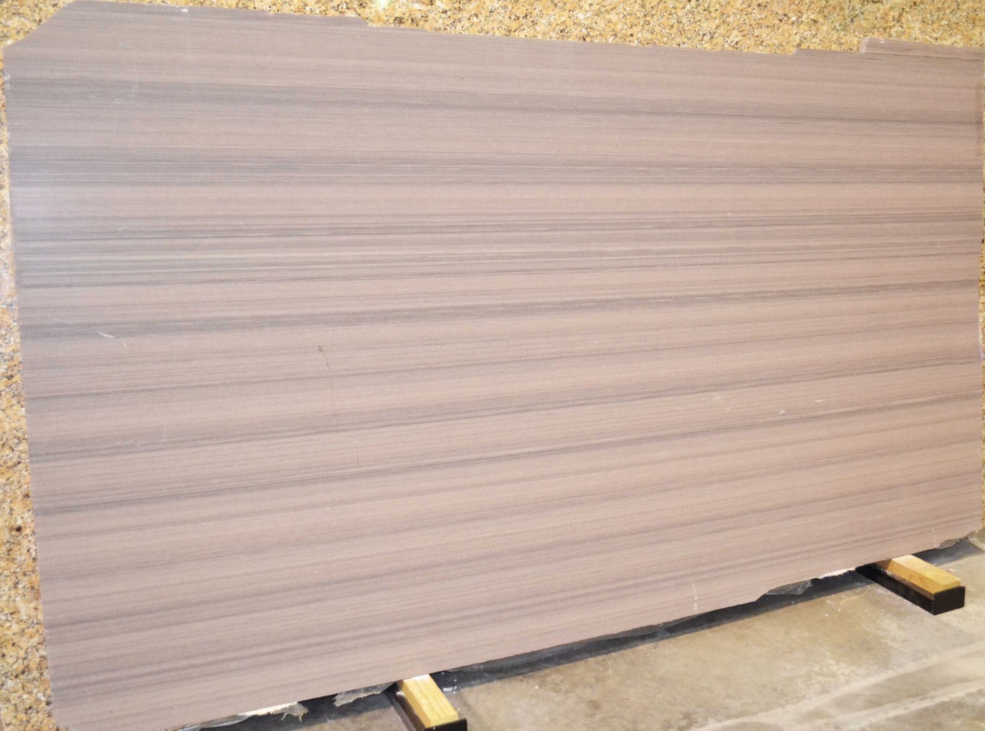 Large slab of light brown stone with horizontal grey veining, propped on wooden supports.