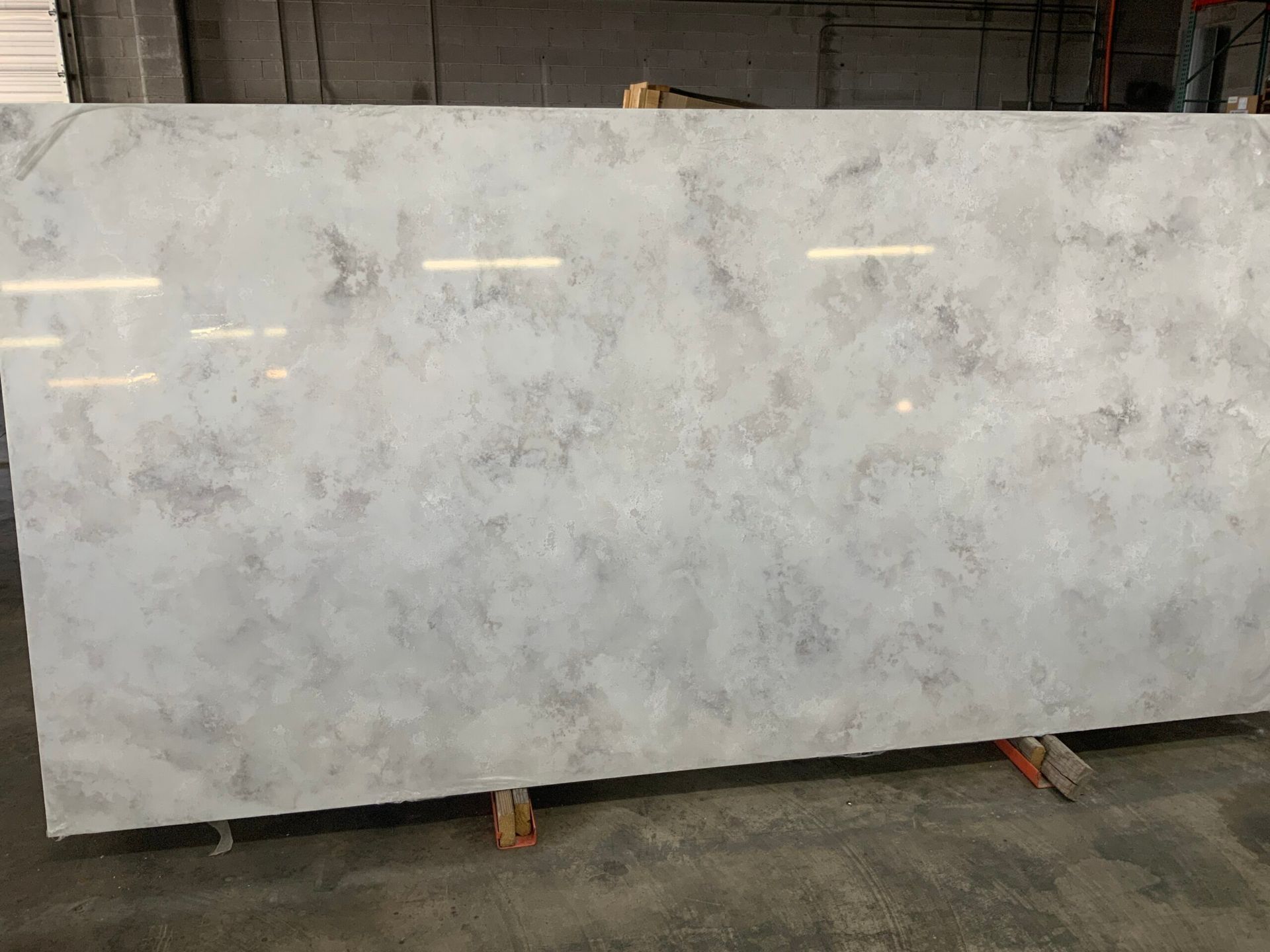 Large, light-colored stone slab with gray and white patterns, resting on wooden supports in a warehouse setting.