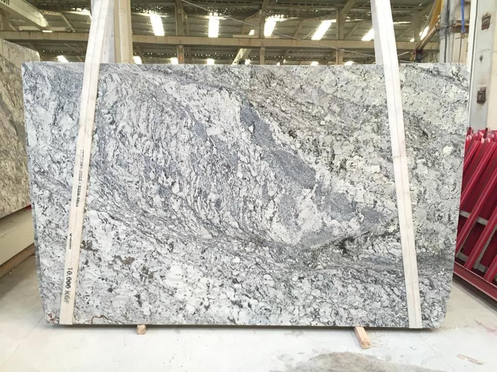 Granite slab, white with gray and black veining, supported by wooden straps in a warehouse.