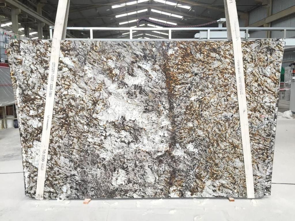 A large granite slab with white, brown, and gray veining, suspended by straps in a warehouse.