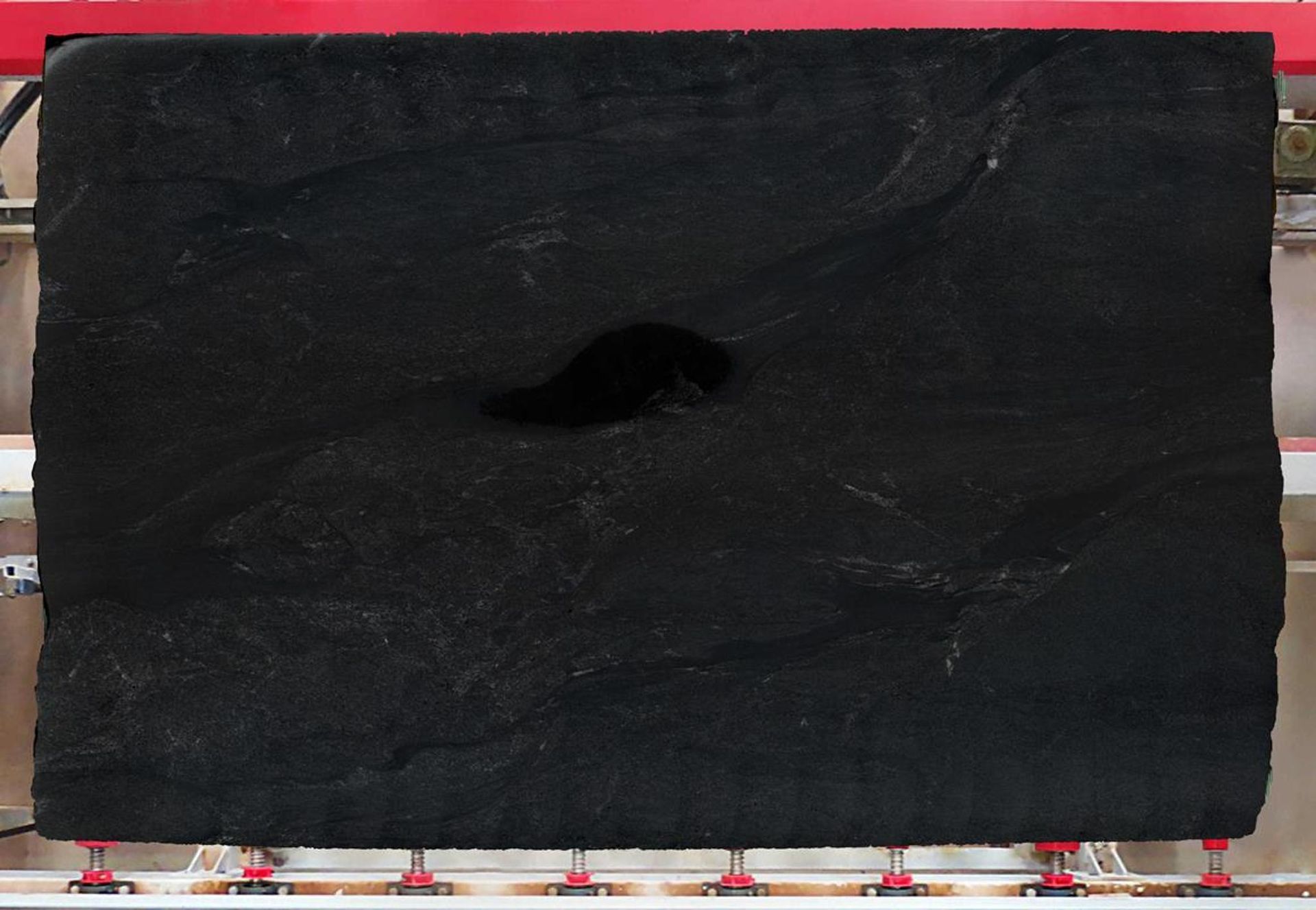 Black slab of stone with a dark void in the center, resting on metal supports.