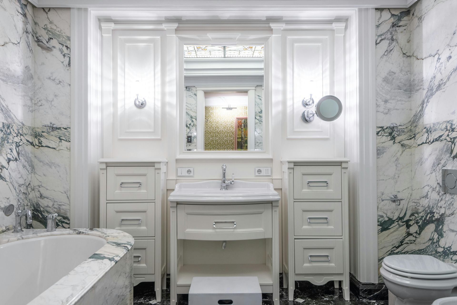 Elegant white bathroom with marble walls, vanity, cabinets, mirror, and toilet.