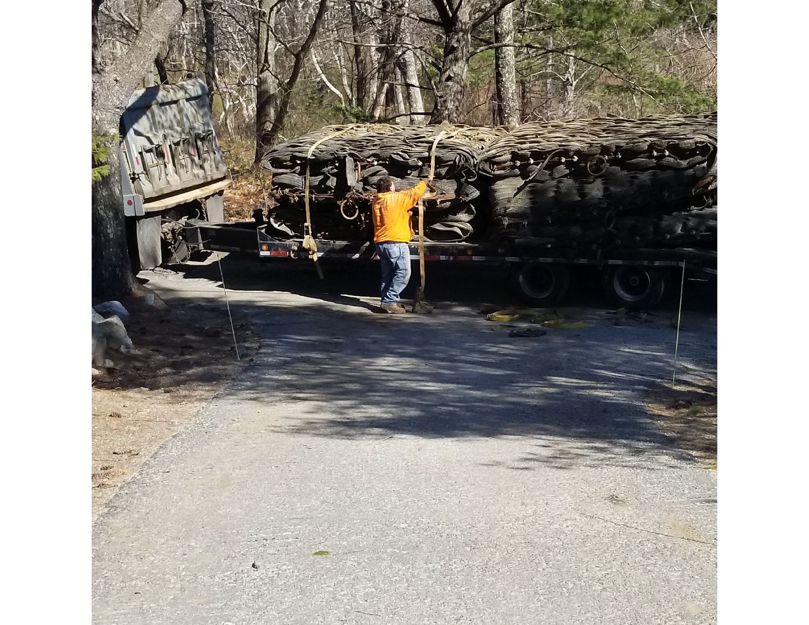 Man in orange shirt by a truckload of stacked rocks. Truck is parked on a gravel road, outdoors, in wooded area.