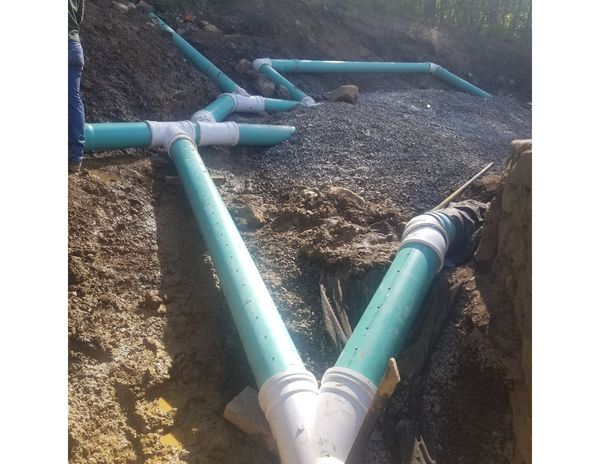 Blue PVC pipes and fittings installed in gravel-filled trenches for a drainage system.