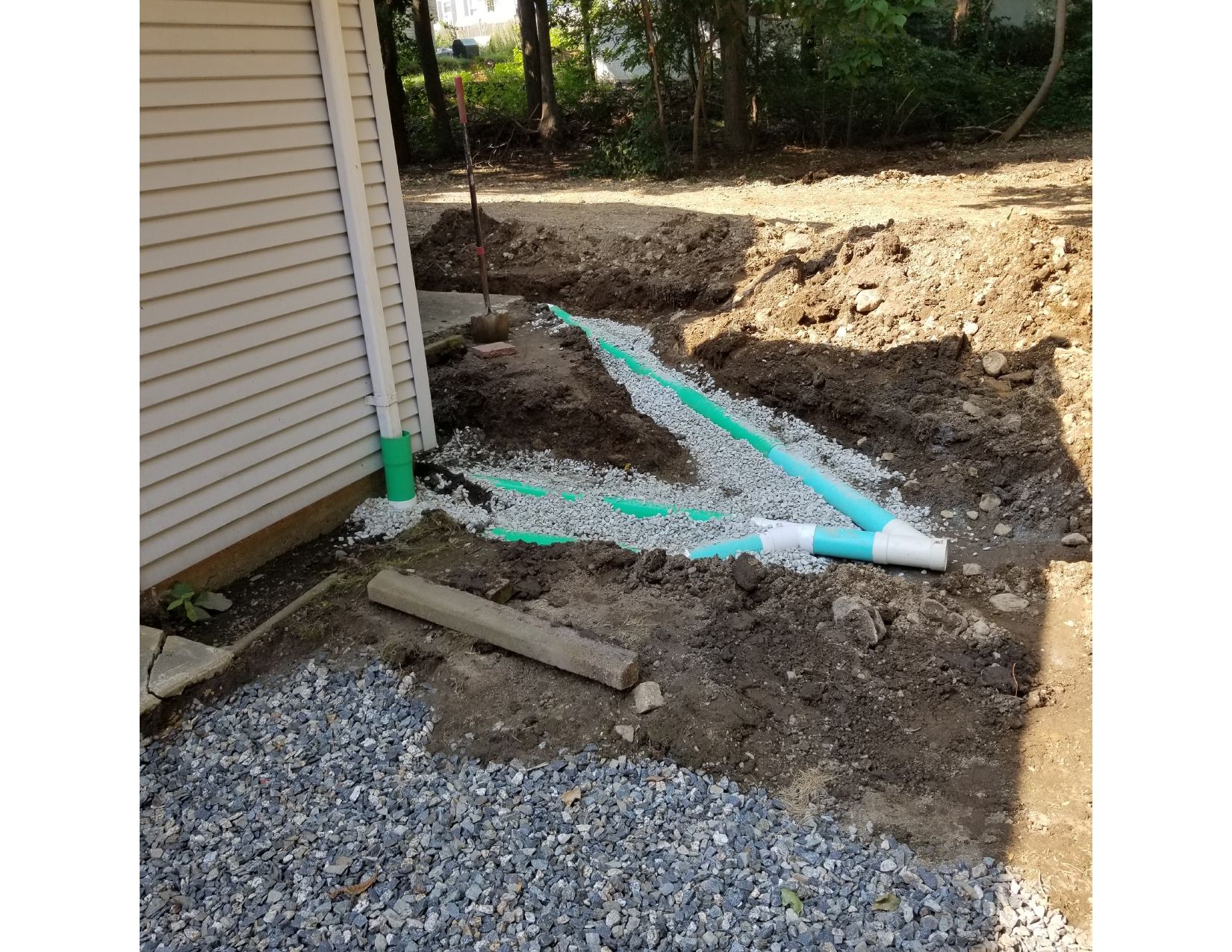 Excavation next to a house with exposed drainage pipes, gravel, and dirt.