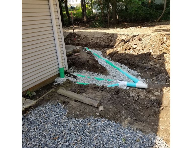 Excavation next to a house with exposed drainage pipes, gravel, and dirt.
