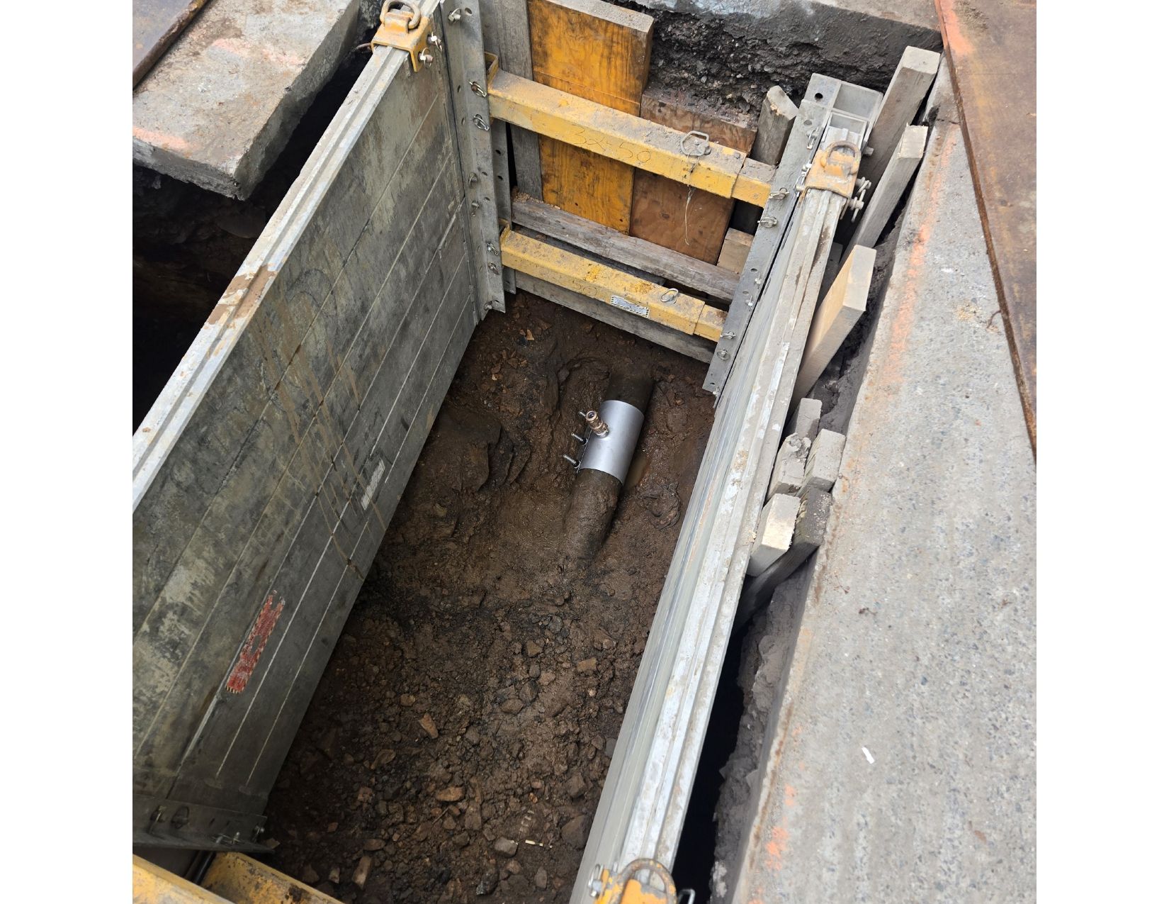 Trench with shoring to protect workers. Silver pipe in the dirt.