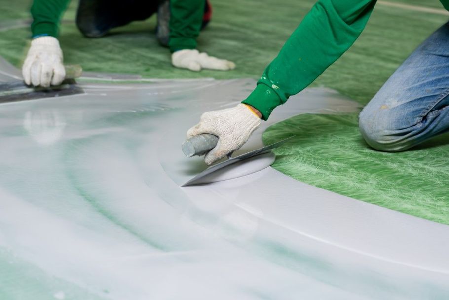 Gloved workers smoothing a white coating over a green floor with trowels