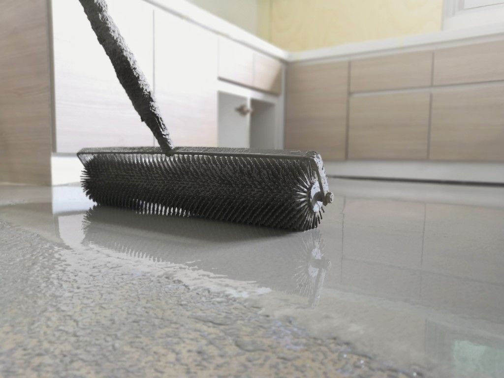 Black roller brush on a glossy kitchen floor beside a white cabinet and beige tiled wall.