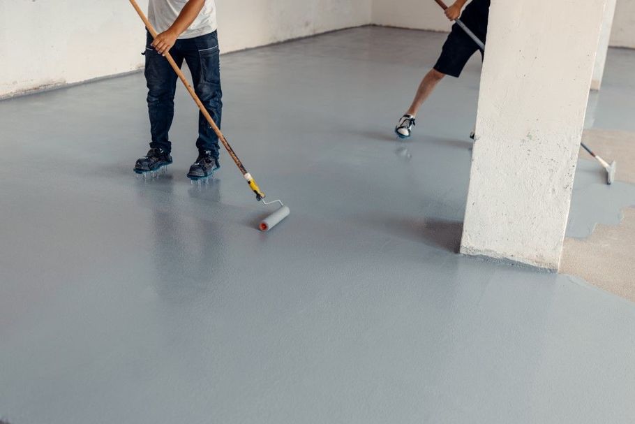 Workers applying gray floor coating with rollers in a room
