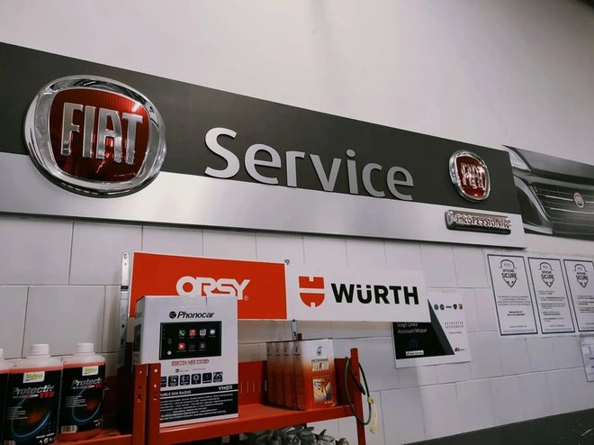 Un'insegna di una stazione di servizio Fiat su una parete, sopra uno scaffale rosso con prodotti per auto e il marchio WURTH.