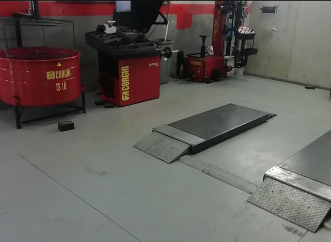 Il pavimento di un'officina meccanica con due sollevatori per veicoli a incasso e attrezzature rosse, tra cui una macchina per pneumatici e un'equilibratrice per ruote.