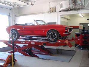 A red car is sitting on a lift in a garage