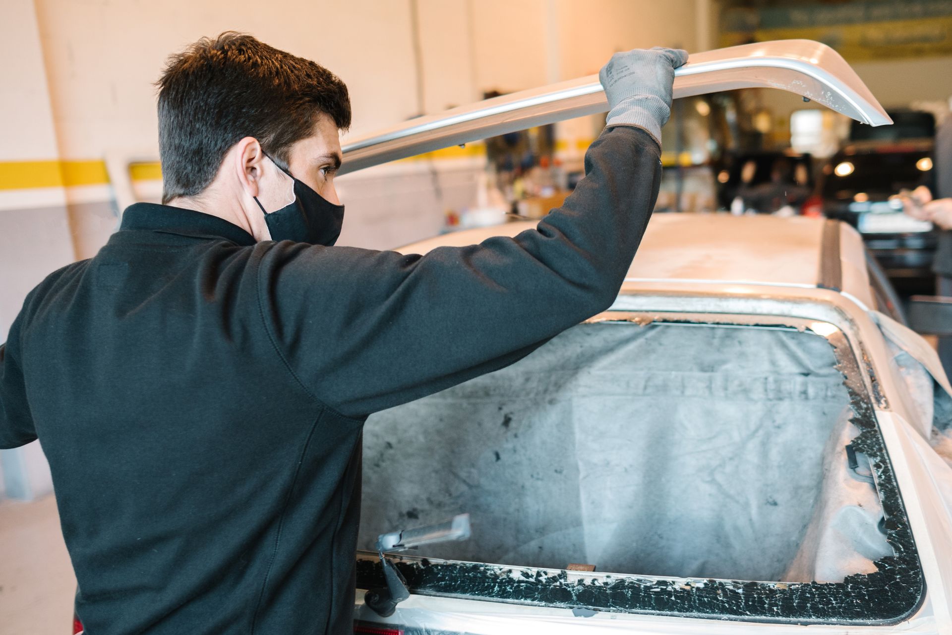 A man wearing a mask is working on a car in a garage.