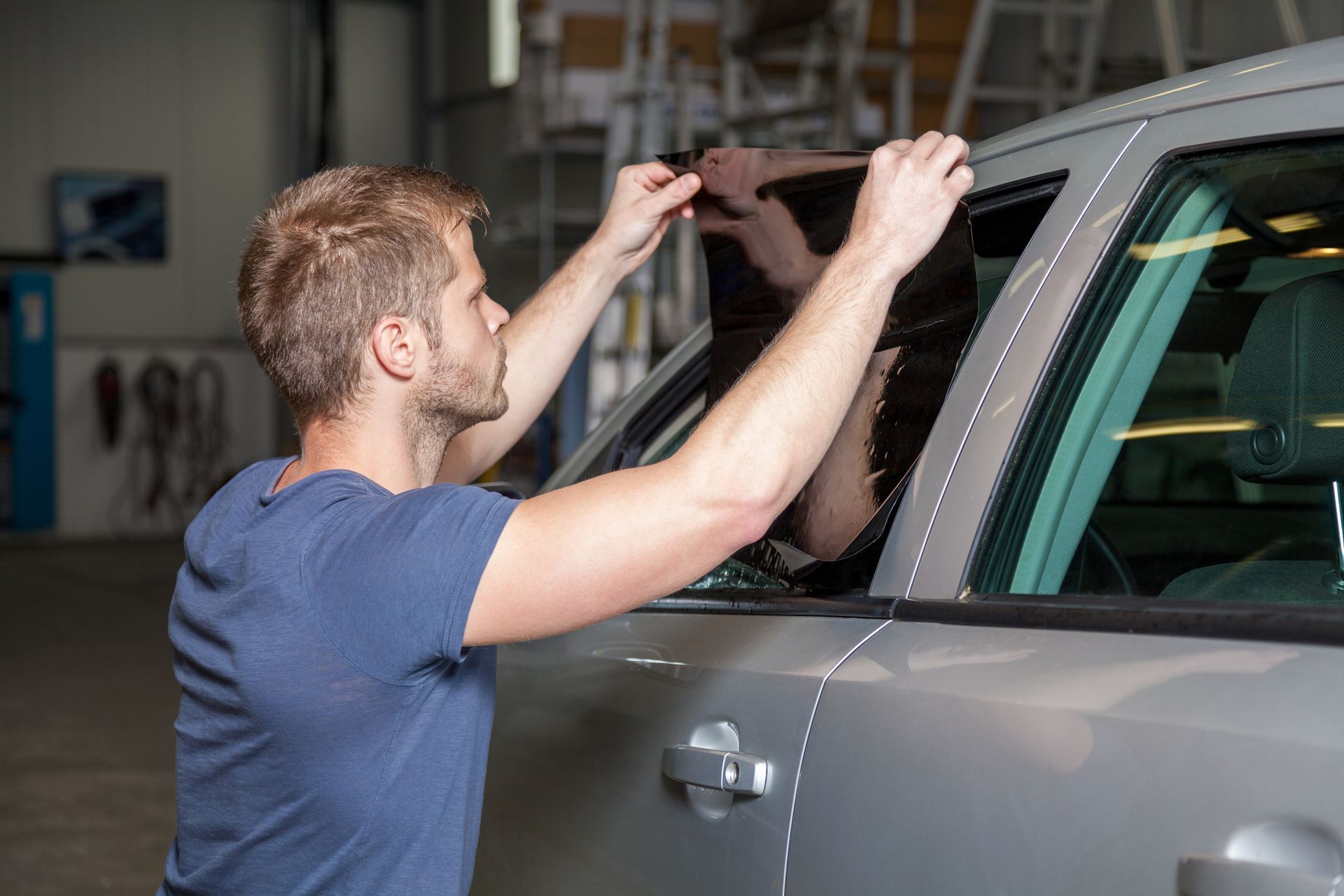 A man is installing tinted windows on a car in a garage.