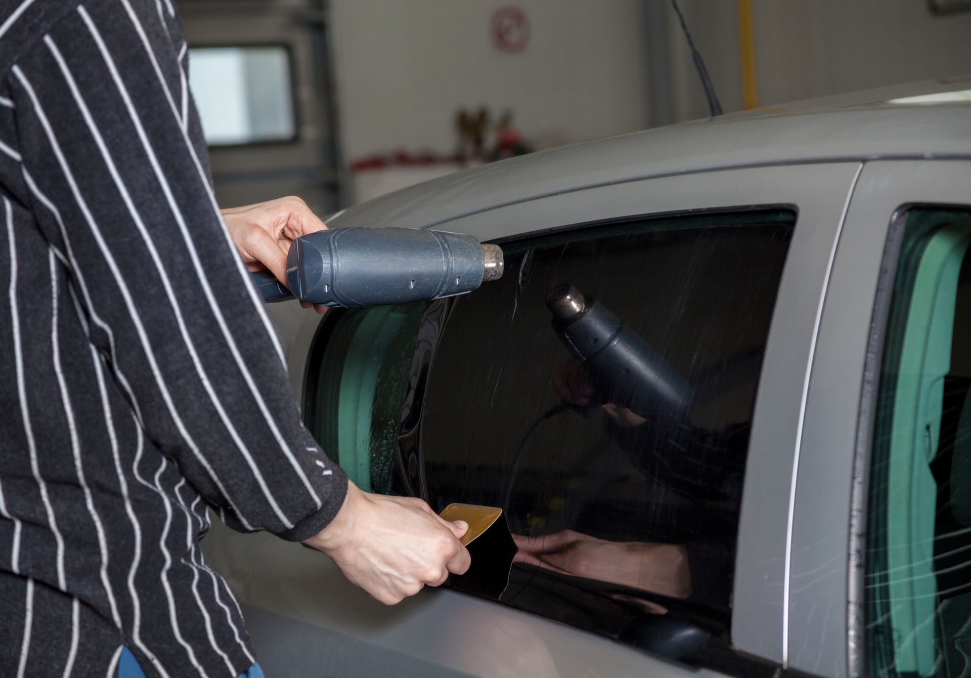 A man is applying tinted window film to a car window.