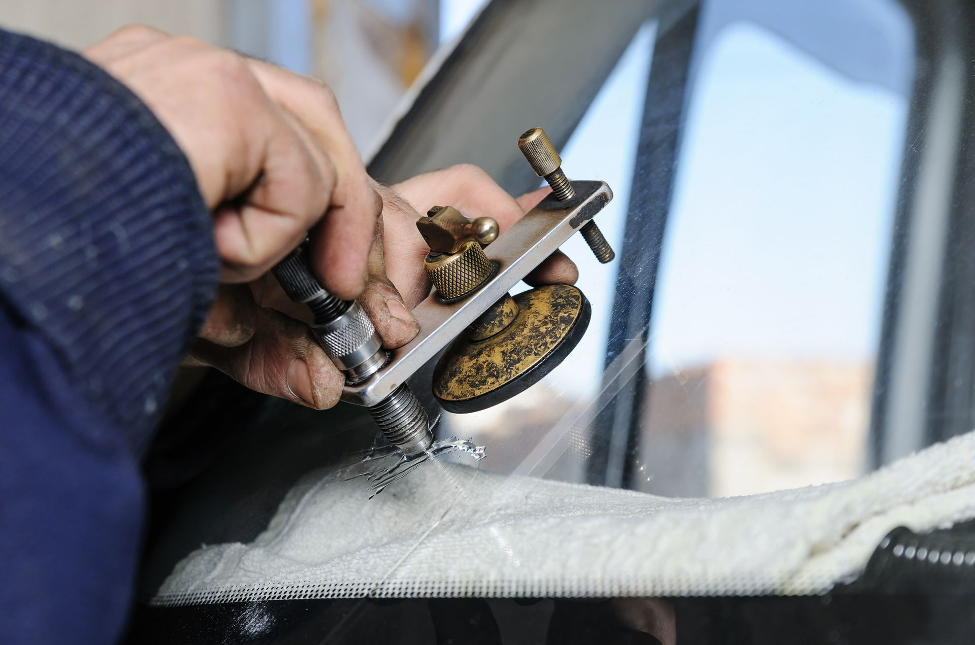 A person is repairing a car windshield with a tool.