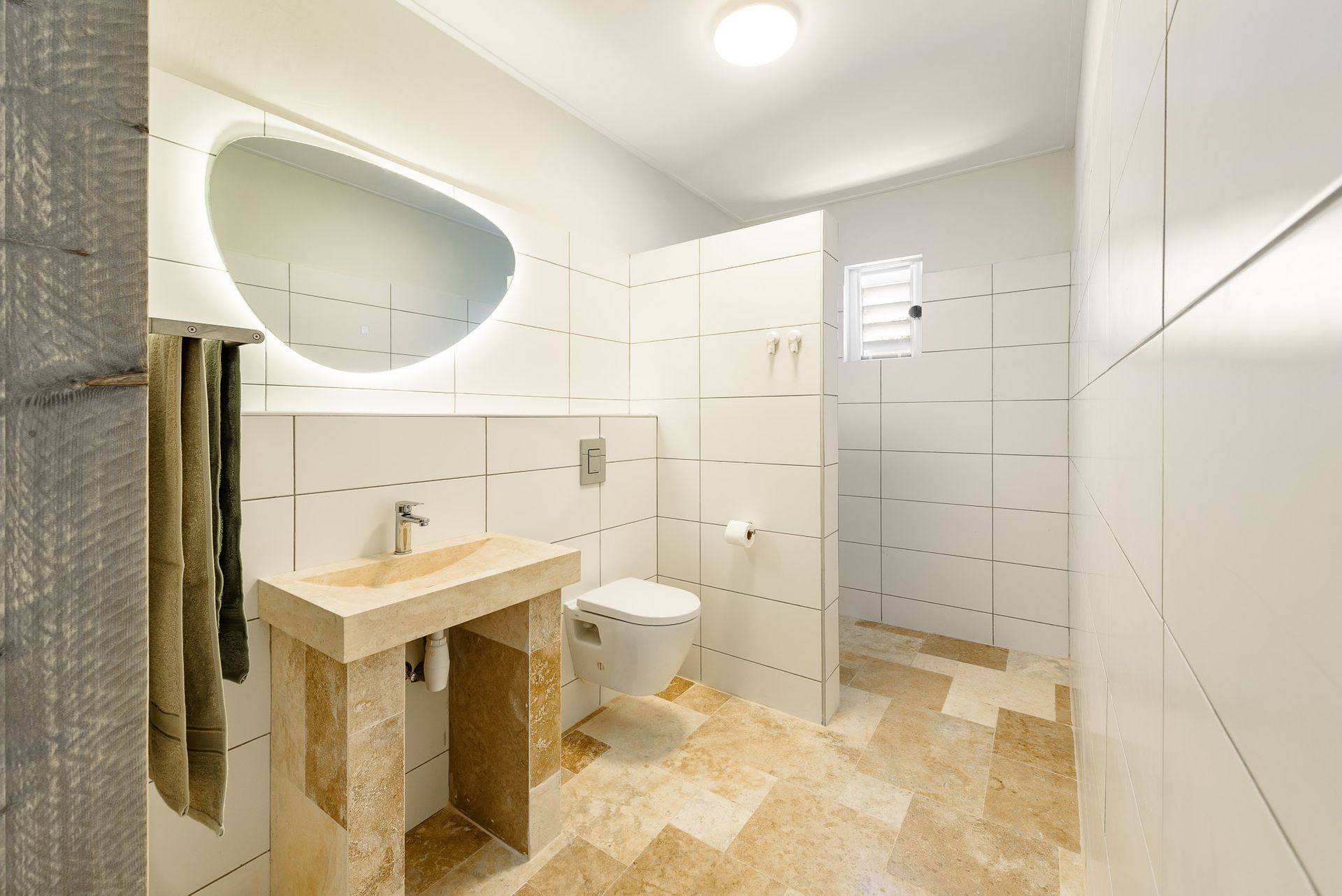 Modern bathroom with a stone sink, a toilet, and a large mirror. Beige tile flooring and white walls.