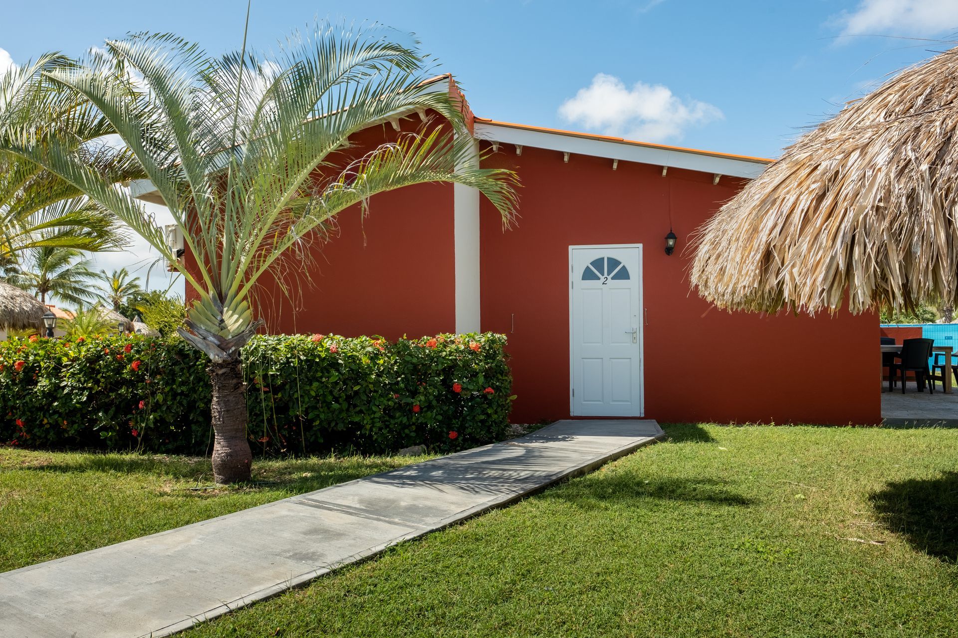 Red building with white door, palm tree, and thatch roof.