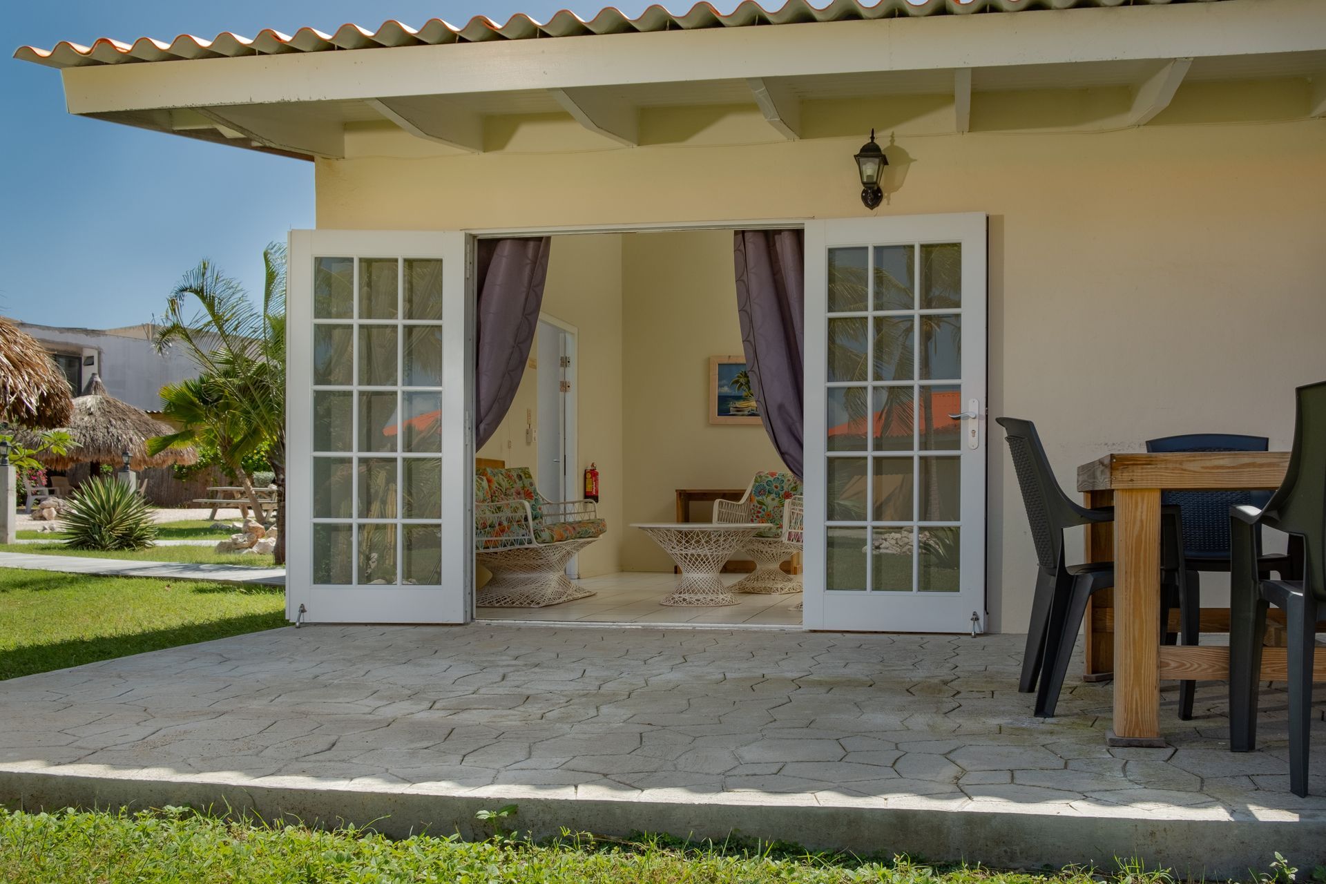 Exterior of a house with open double doors, leading to a patio with a table and chairs.