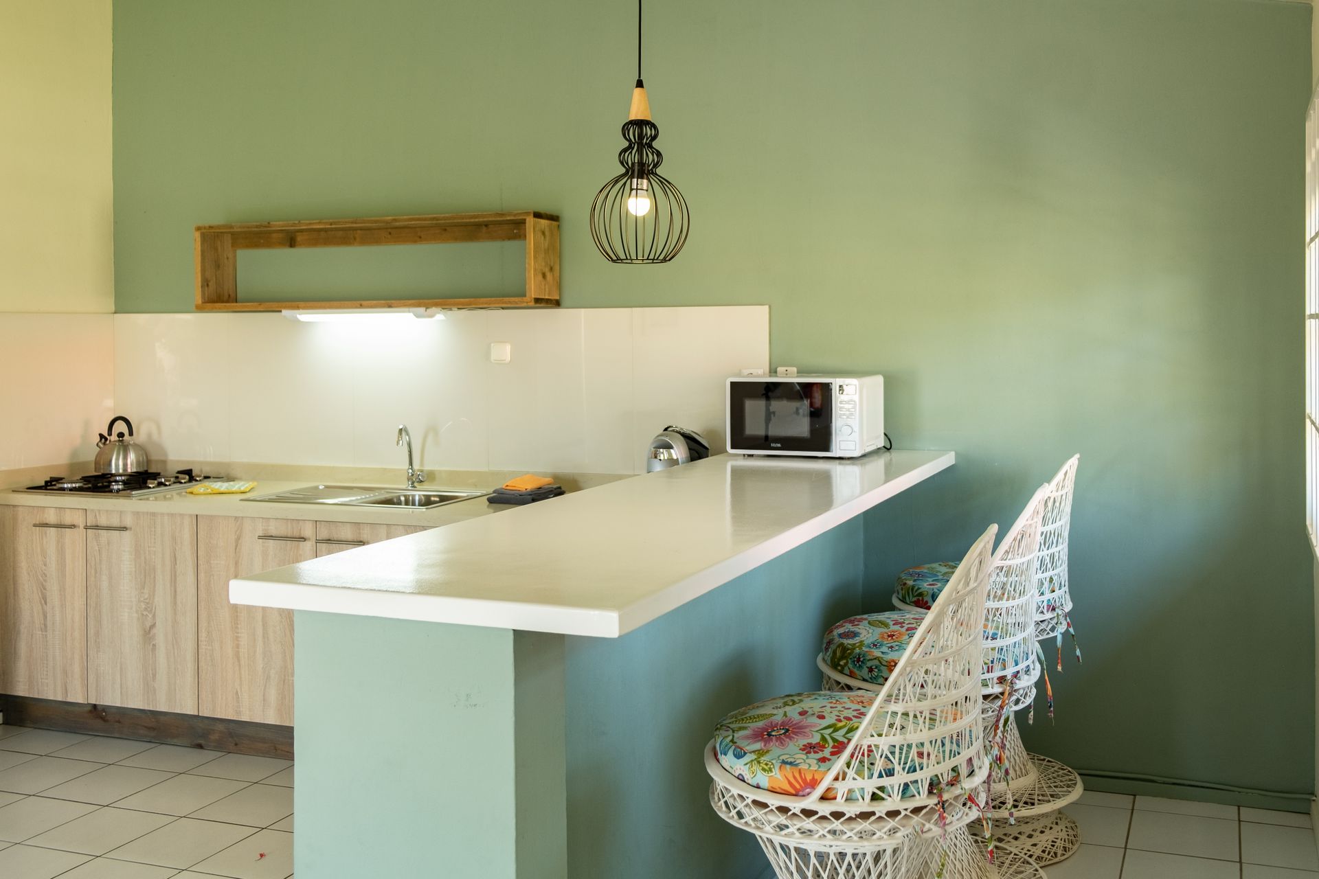 Kitchen with light wood cabinets, white counter, microwave, and decorative hanging light fixture.