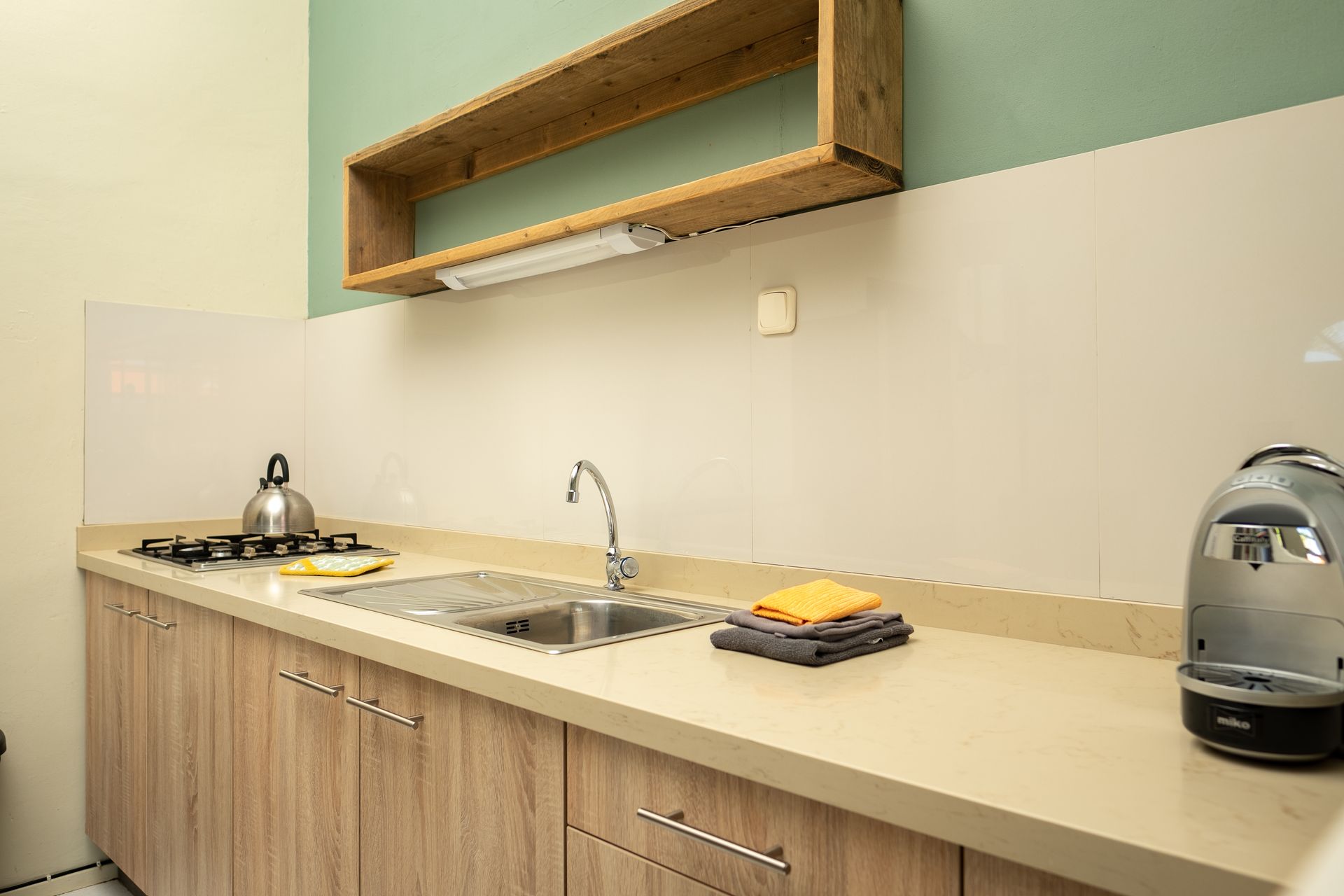 Kitchen with light wood cabinets, beige countertop, stainless steel sink, gas stove, and teapot.