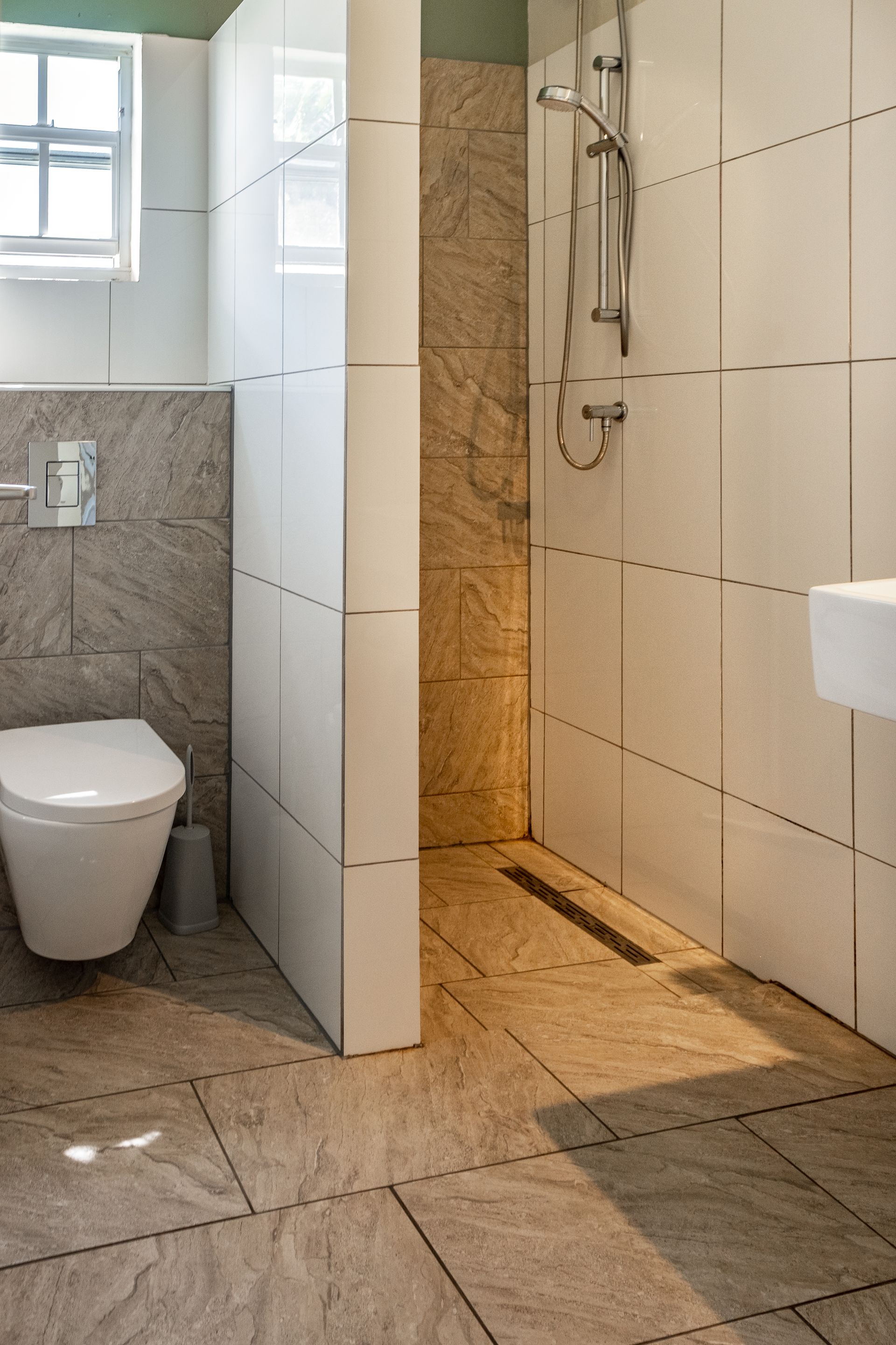 Modern bathroom with shower stall, toilet, and light-colored tile.