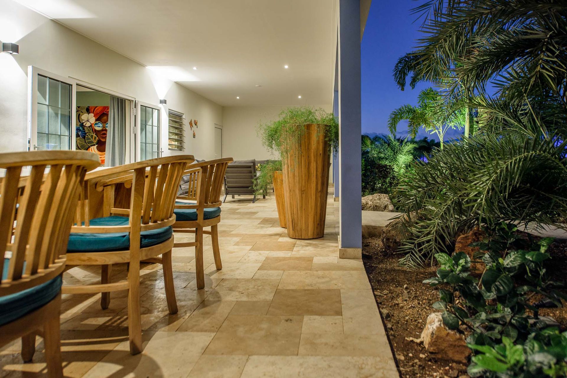 Patio with wooden chairs, large planter, and lush greenery at dusk.
