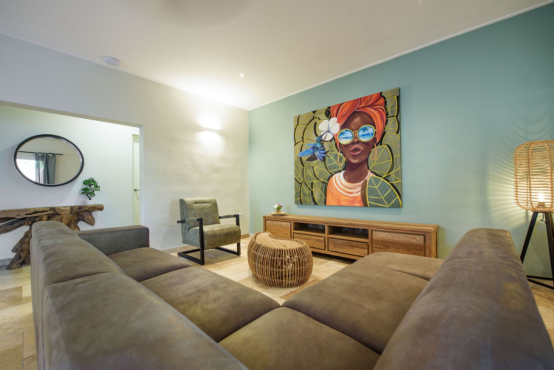 Living room with teal wall and colorful artwork above a wooden TV stand. A gray sectional and a wicker lamp are visible.
