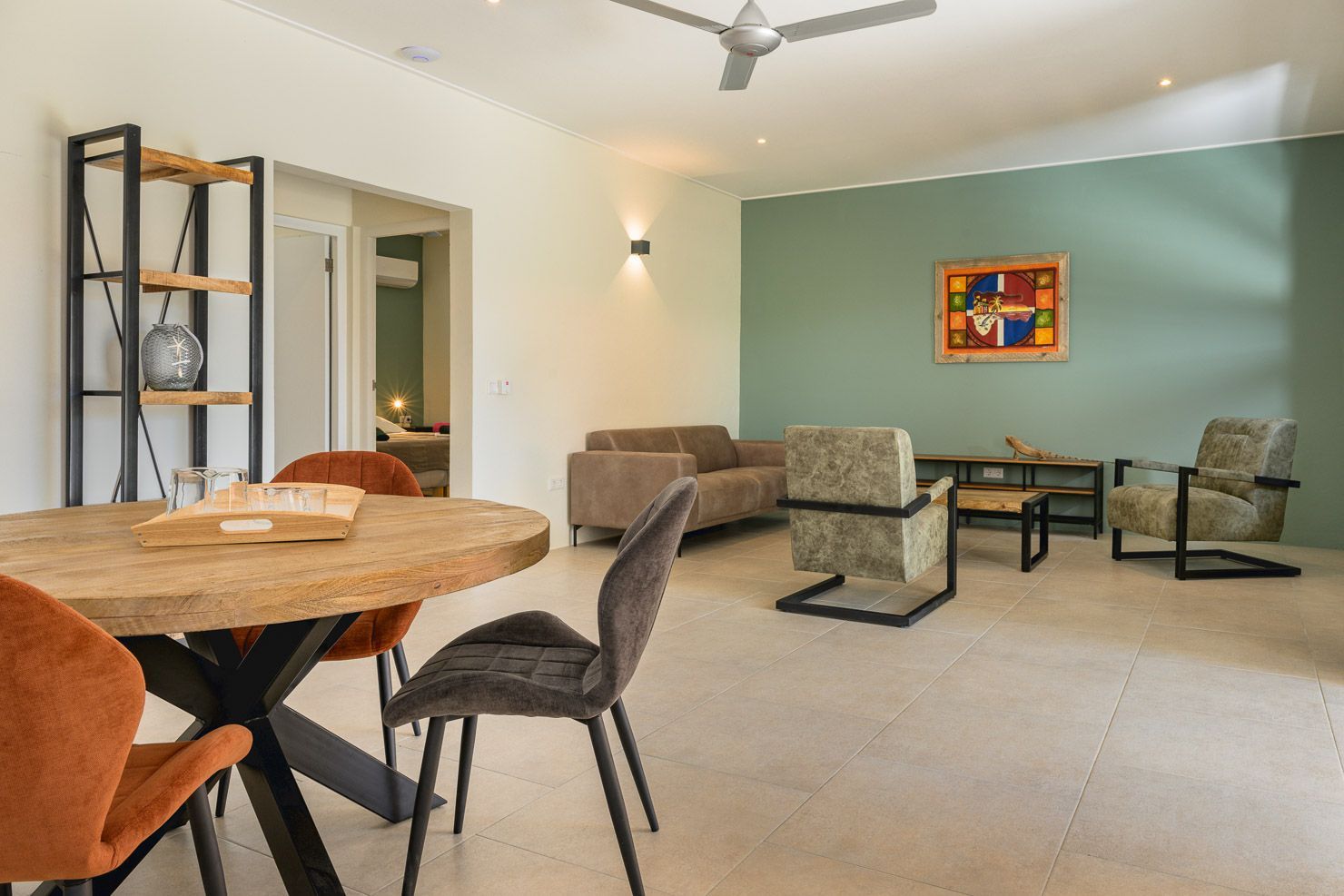 Living room with round dining table, sofa, chairs, and artwork on green wall.