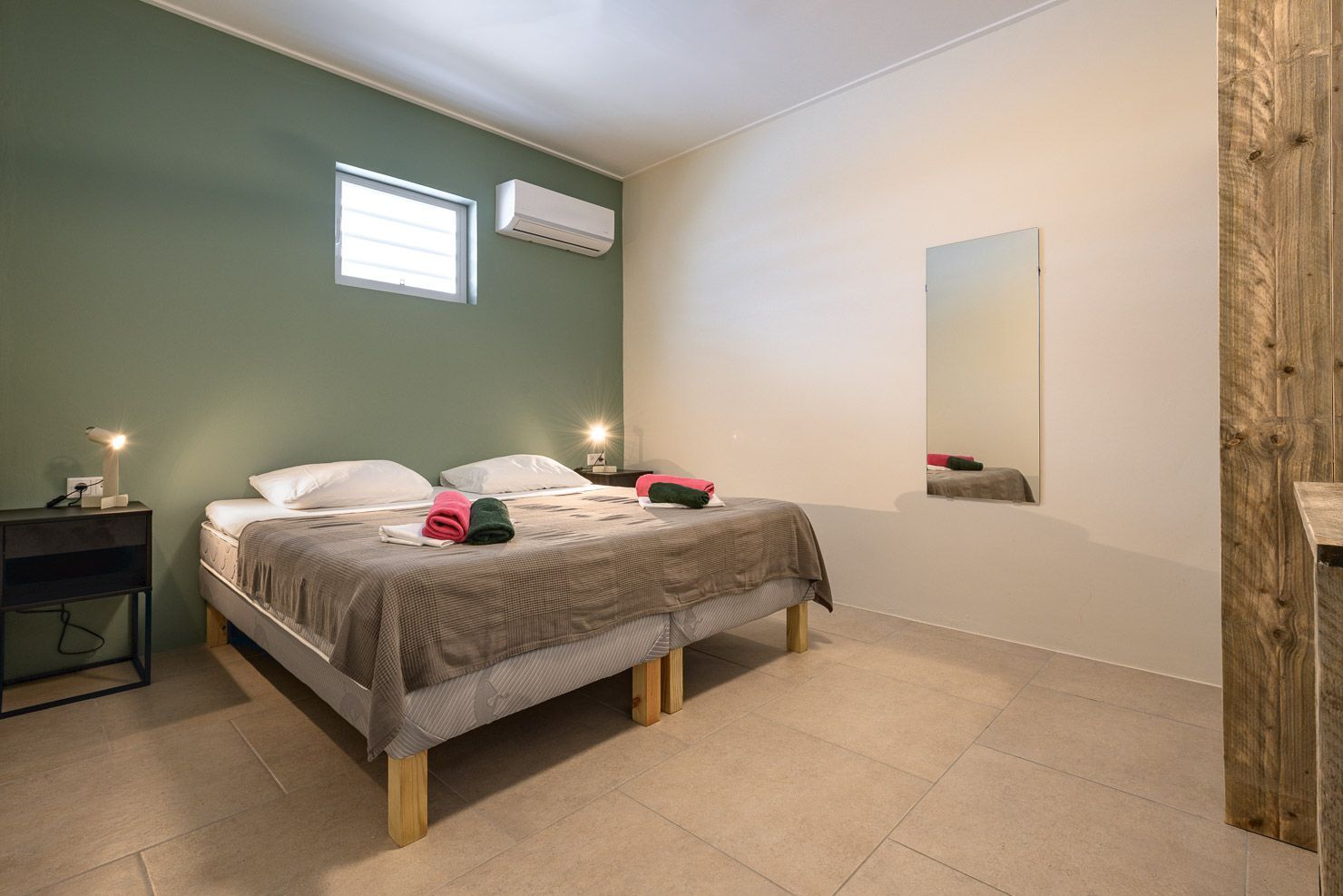 Bedroom with two beds, green and beige walls, window, mirror, and wooden trim.