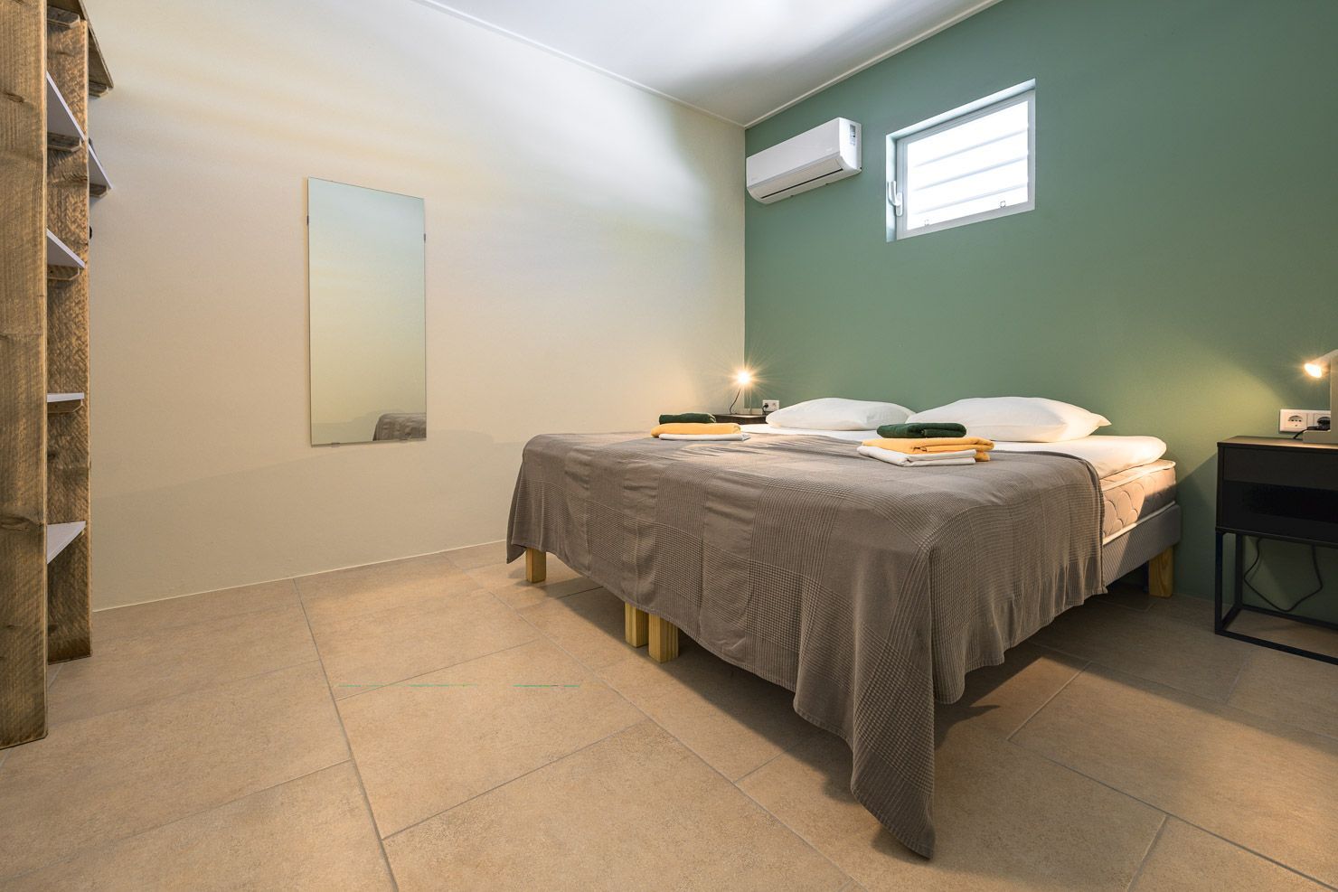 Bedroom with gray bed, green accent wall, wooden shelving unit, and air conditioner.