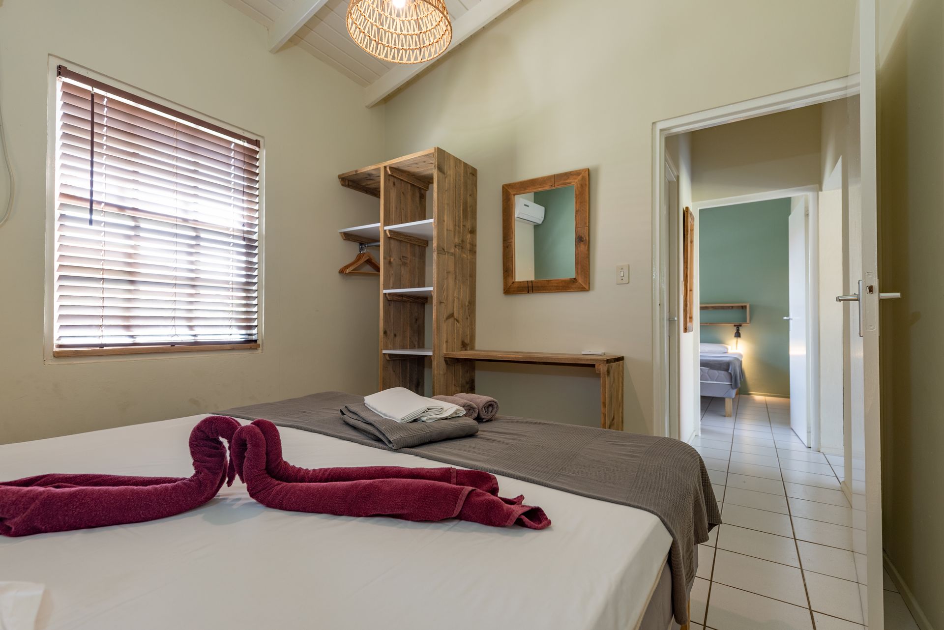 Bedroom with a bed, wooden wardrobe, mirror, and a doorway to another room.