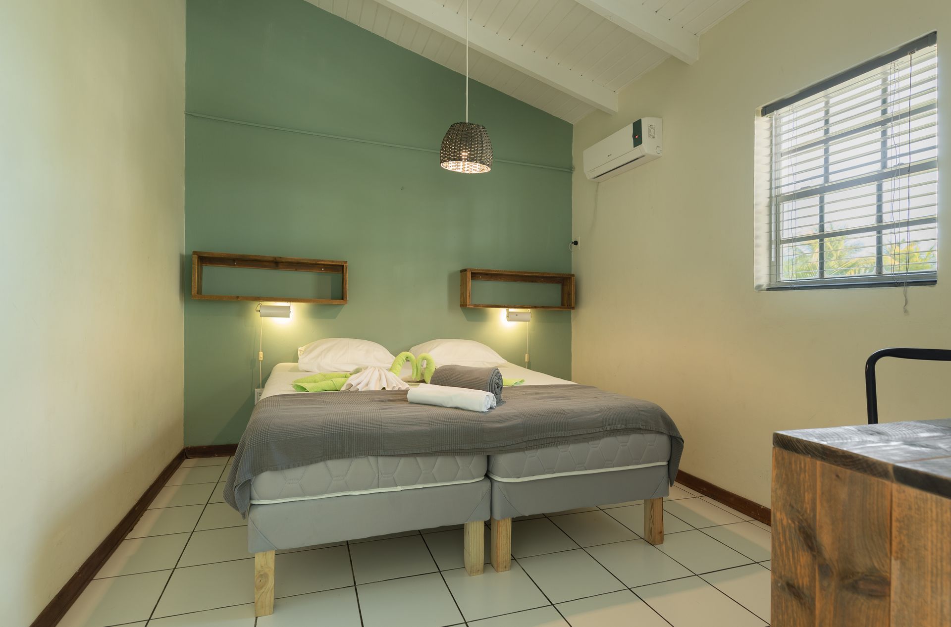 Bedroom with two beds, green accent wall, wooden shelves, window, white tile floor.