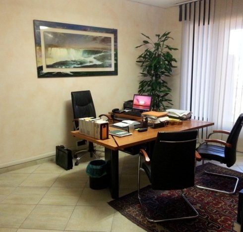 Ufficio con scrivania, sedie, opere d'arte, piante e finestra con persiane.