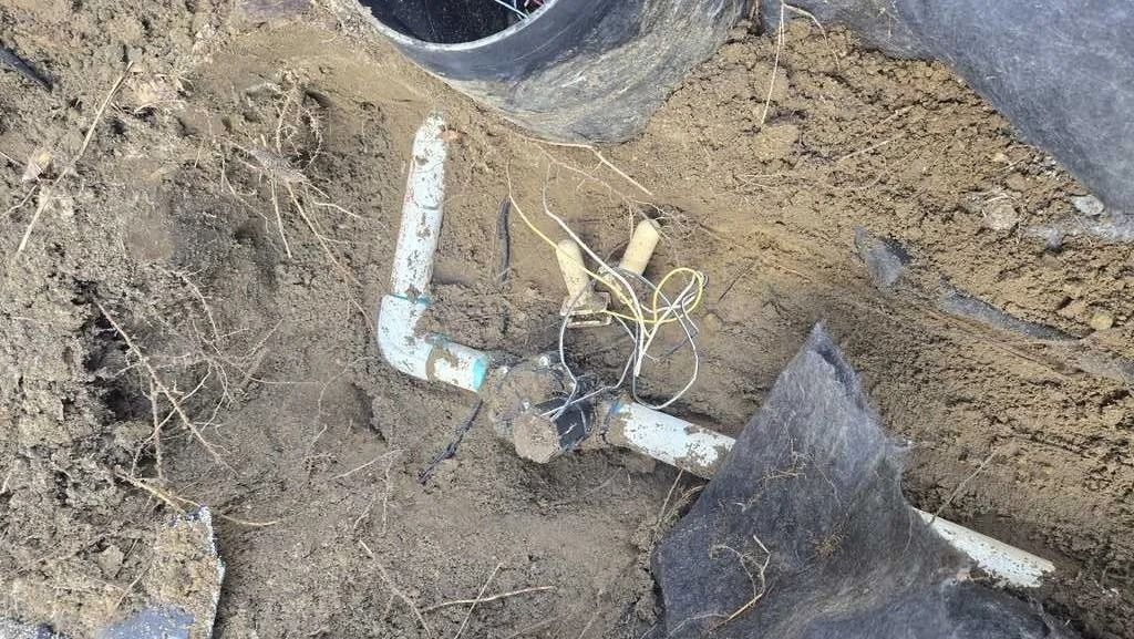 White PVC pipes and a black tarp buried in dirt at a construction site