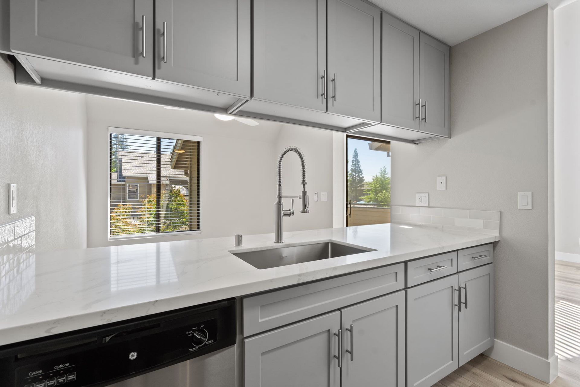 Modern kitchen with gray cabinets, marble-look countertop, and stainless steel sink.