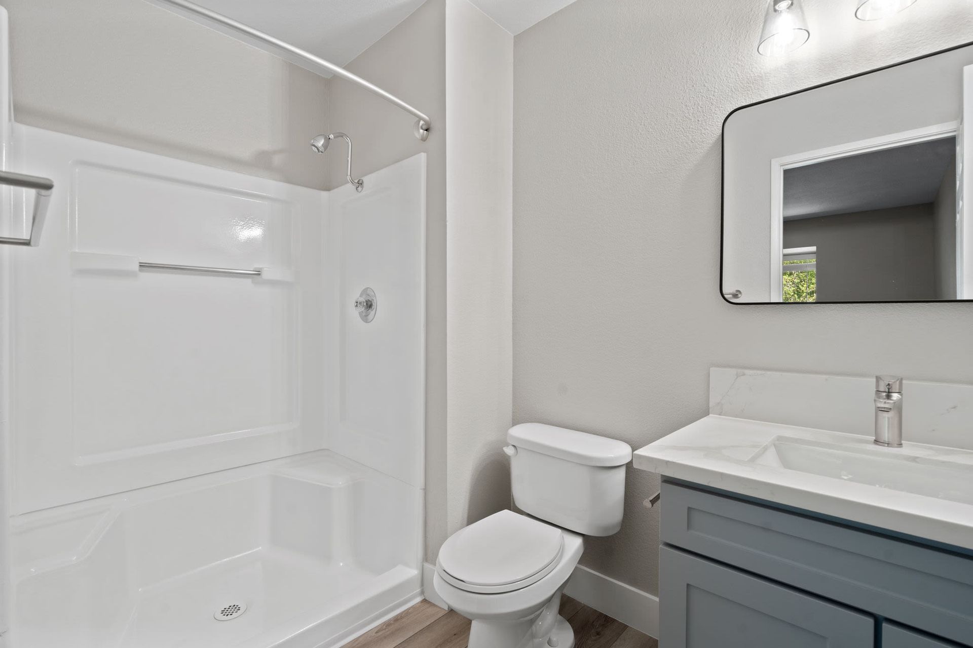 Bright bathroom with a white shower-tub, toilet, and gray vanity.